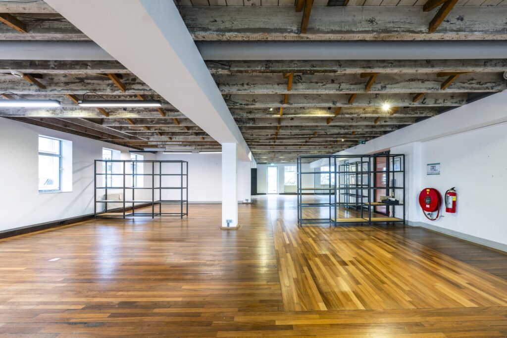 Ruime, industriële kantoorruimte aan de De Ruijterkade met houten vloer, zichtbare plafondbalken en metalen stellingkasten.